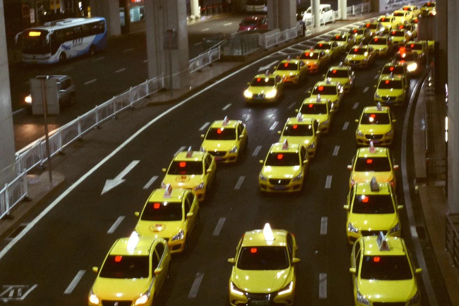 File de taxis d’une même compagnie roulant de front sur une avenue, de nuit