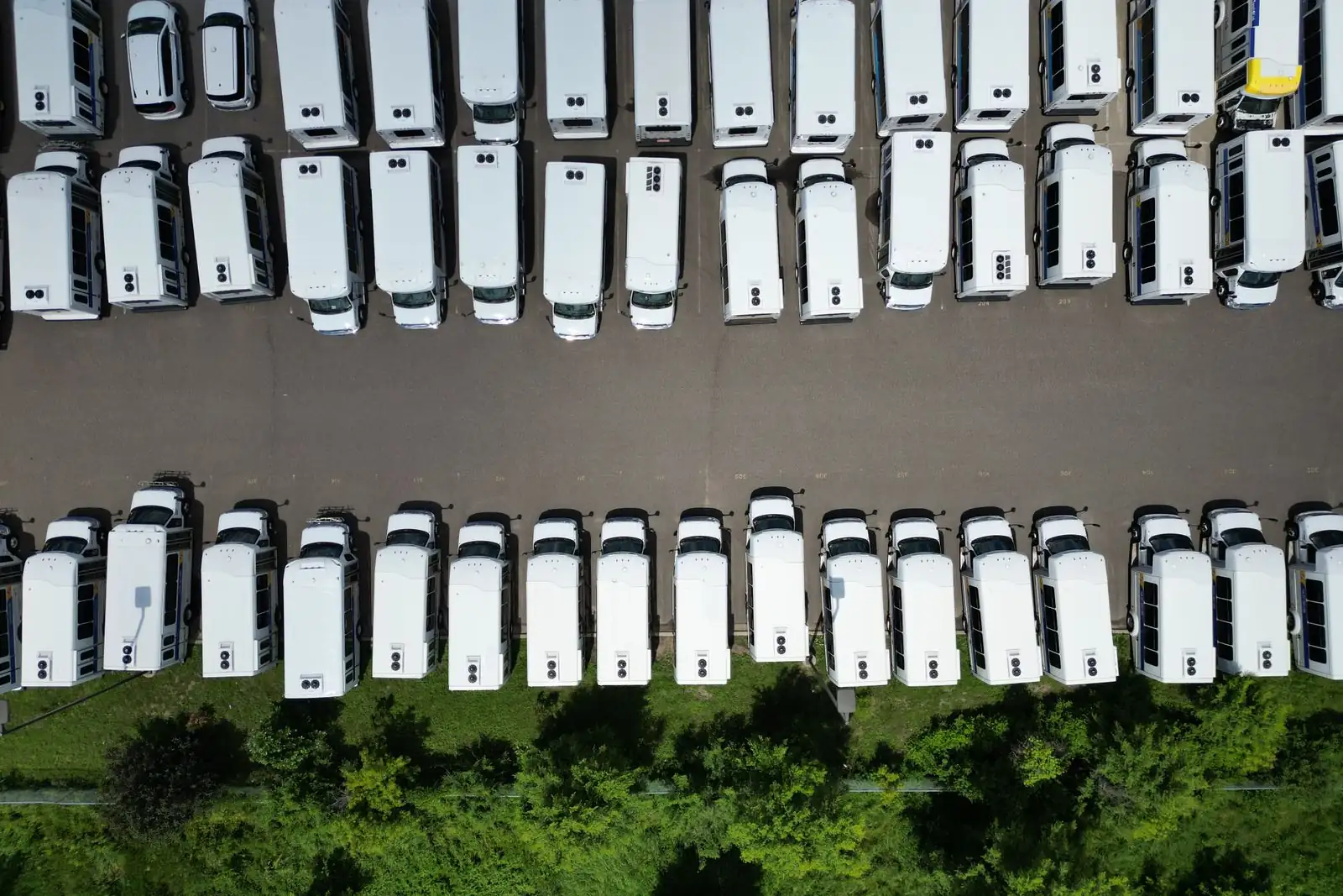 Vue aérienne de fourgons utilitaires blancs d’une entreprise stationnés en rangées sur son parc